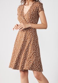 Braun gepunktetes Kleid aus weichem Stoff, mit einem V-Ausschnitt und kurzen Ärmeln. Das Kleid ist an der Taille weit geschnitten und hat einen knielangen Saum.