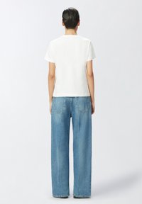 Camiseta blanca de manga corta combinada con jeans de cintura alta y pierna ancha de color azul. Los jeans de mezclilla tienen bolsillos traseros y una textura ligeramente desgastada.