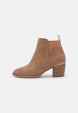 Brown suede ankle boot with stacked block heel, elastic side panel, and textured heel detail on neutral background.
