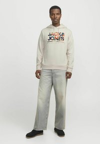 Sudadera con capucha gris con el logotipo de "JACK & JONES" en negro y naranja, combinada con jeans de pierna ancha de lavado claro y zapatillas negras.