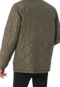 Quiltad olivgrön jacka med vågmönstrad textur, långa ärmar och en avslappnad passform. Har en rundad nederkant och minimal hårdvara.