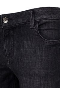 Jeans en denim fonc é avec une vue en gros plan mettant en évidence la texture du tissu, le bouton en métal et la petite poche à pièces près de la taille.