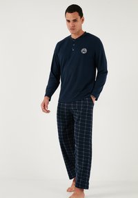 Cămașă henley cu mâneci lungi de culoare bleumarin, cu deschidere la gât cu butoane și logo, asortată cu pantaloni de pijama cu carouri bleumarin. Material moale și respirabil; croială relaxată.