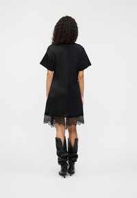 Μαύρο φόρεμα με κοντά μανίκια και δαντελένιο τελείωμα. Ομαλό ύφασμα με ίσια γραμμή. Φορεμένο με μαύρες μπότες έως το γόνατο που έχουν σχέδιο σε σχήμα V.