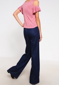 Pink cold-shoulder top with ruffled sleeves paired with navy flared trousers. The fabric appears soft with a smooth texture and a fitted design.
