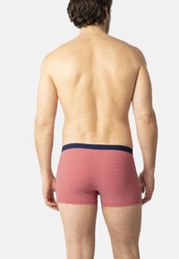 Shorts de boxer rouges à motif avec une ceinture marine, présentant un design texturé et une coupe ajustée. Exposés sur un dos nu.