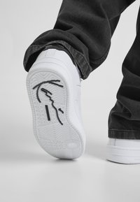 Valge tossu tekstuurse kummitaldiga, millel on allosas mustaks aksendiks kujundus, kombineeritud tumehallide teksapükstega.