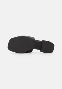 Svart sko med en strukturerad sula, bred klack och slätt övermaterial. Har en minimalistisk design med rundad tå.