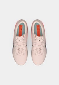 Ténis de desporto rosa-claro com um padrão texturizado, logótipo Swoosh preto, atacadores brancos e detalhes corais no calcanhar e na sola.