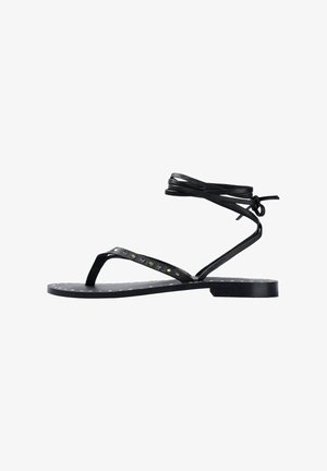 Sandales noires à lanières avec une semelle plate, ornées d'accents en clous sur les lanières, avec une attache autour de la cheville et une texture lisse.