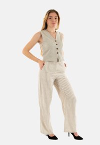 Chaleco sin mangas color beige con rayas verticales y botones de madera, combinado con pantalones de pierna ancha a rayas a juego. Tacones negros completan el conjunto.