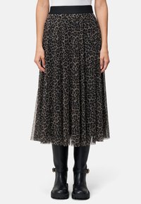 Plisseret midnederdel i gennemsigtigt sort stof med et leopardprintdesign, forsynet med en sort elastisk talje og båret med sorte knæhøje støvler.