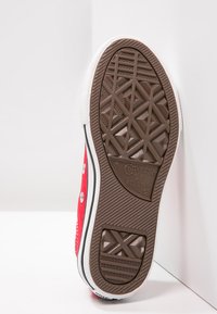 Rote Leinensneaker mit weißer Gummikappe und Sohle. Die Unterseite verfügt über eine strukturierte braune Gummisohle mit einem gemusterten Profil für zusätzlichen Halt.