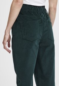Dark green corduroy pants with an elastic waistband, featuring two back pockets and a soft, textured fabric. No visible hardware.