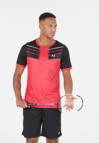 Punainen ja musta urheilupaita lyhyillä hihoilla, jossa on vaakasuoria raidoja ja logo. Yhdistetty mustiin shortseihin; pitämällä sulkapallomaila.