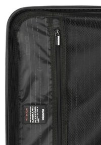 Intérieur d'un bagage de voyage noir avec une poche zippée, texture en mailles et une étiquette de marque. Le tissu est durable avec un motif subtil.
