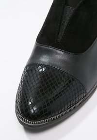 Chaussure en cuir noir et daim avec bout en cuir à motif de peau de serpent texturé et brillant et panneau latéral élastique.