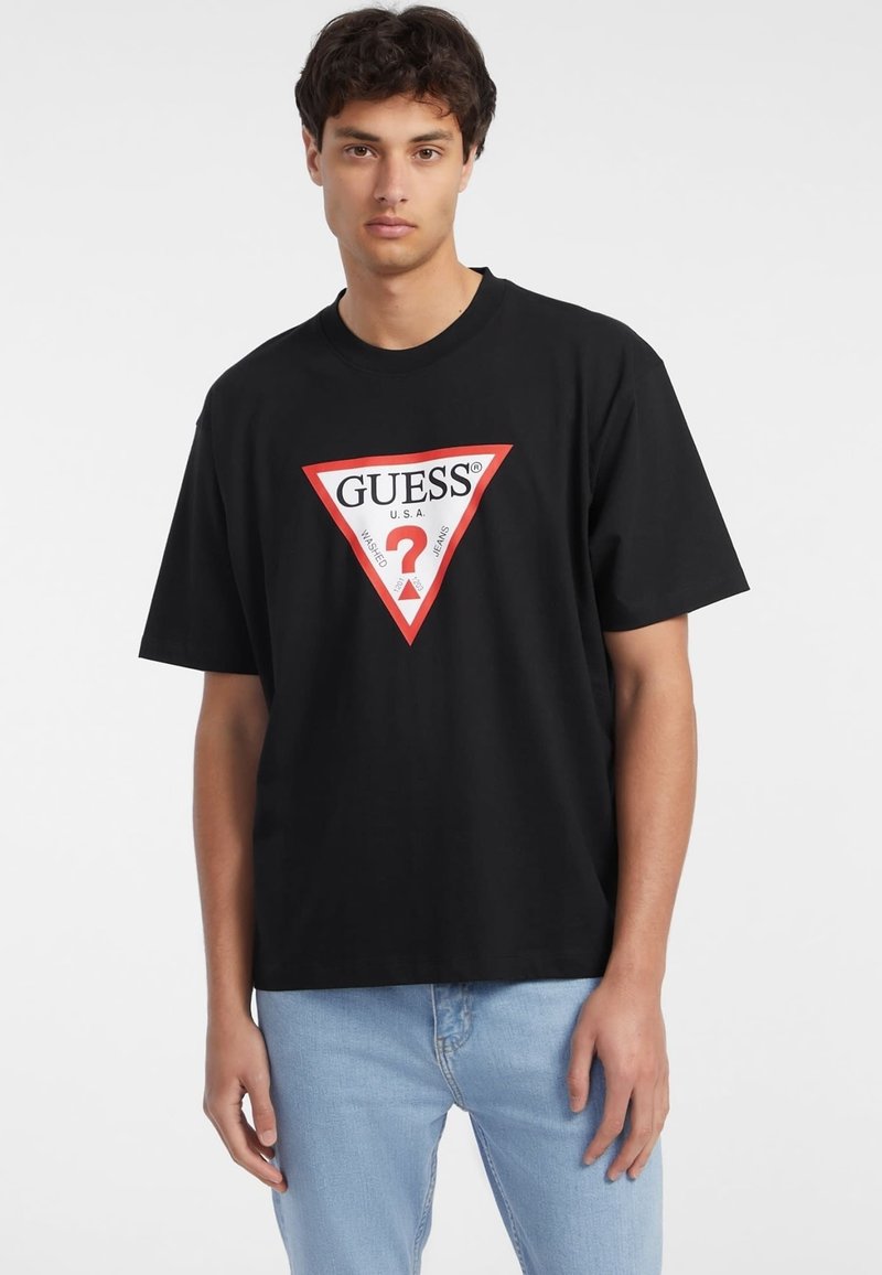 Juodas medvilnės marškinėliai trumpomis rankovėmis, su dideliu raudonu trikampiu logotipu, kuriame parašyta "GUESS U.S.A." ir viduje yra baltas klausimo ženklas.