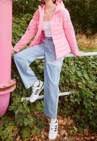 Pinkki toppatakki hupulla, valkoinen paita, siniset leveälahkeiset farkut, joissa kontrastivärisiä tilkkuja, ja mustavalkoiset lenkkarit raidoilla.