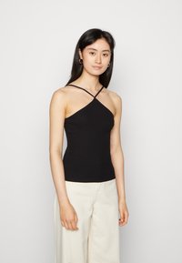 Top preto sem mangas com alças cruzadas, apresentando um design ajustado e uma textura suave. Combinado com calças largas de cor clara.