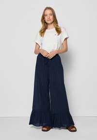 Biały top z krótkim rękawem z haftem kwiatowym i falbankami, zestawiony z granatowymi spodniami szerokimi z pionowymi paskami i falbaną u dołu.