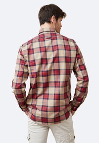 Camisa de cuadros con una gama de colores en beige, rojo y azul marino. Manga larga, puños con botón y un diseño de collar clásico. Textura de tela suave.