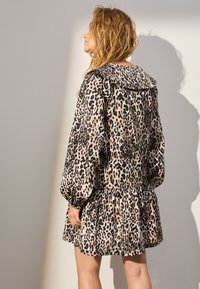 Vestito con stampa leopardata, collo arricciato, maniche lunghe a sbuffo e gonna a balze. Realizzato in tessuto leggero nei colori beige e nero.