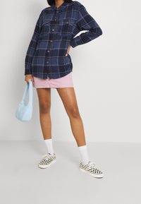 Camicia di flanella a quadri navy con due taschini sul petto, abbinata a una mini gonna di jeans rosa. Calzini bianchi e sneakers a scacchi completano il look.