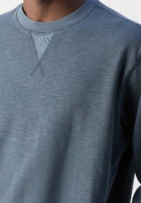 Blauw langarm shirt van textuurstof. Heeft een geribde ronde hals en versterkte stiksels op de halslijn en schouders.