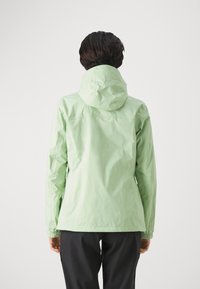Giacca impermeabile verde chiaro con cappuccio, polsini elasticizzati e design aderente, realizzata in tessuto liscio e leggero.
