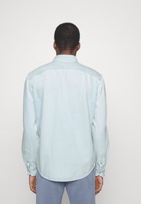 Camicia di jeans azzurra con maniche lunghe, orlo arrotondato, polsini con bottone e yoke posteriore. Tessuto liscio con leggeri sbiadimenti.