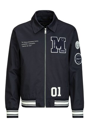 Marineblaue Reißverschlussjacke mit weißen Collegestyle-Aufnähern, gestreiften Bündchen und Saum, Text auf der linken Brust und runden Aufnähern am rechten Ärmel.