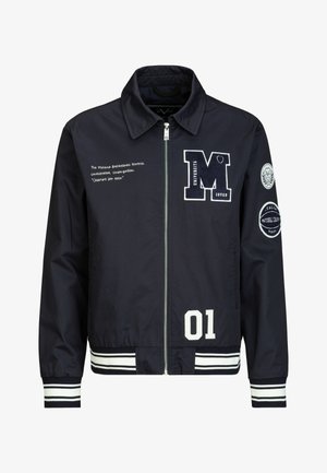 Marineblaue Reißverschlussjacke mit weißen Collegestyle-Aufnähern, gestreiften Bündchen und Saum, Text auf der linken Brust und runden Aufnähern am rechten Ärmel.
