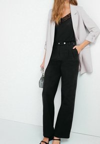 Pantalons noirs taille haute avec plis, un blazer gris élégant et un haut noir avec une touche de dentelle. Fermeture à boutons en argent détaillée.