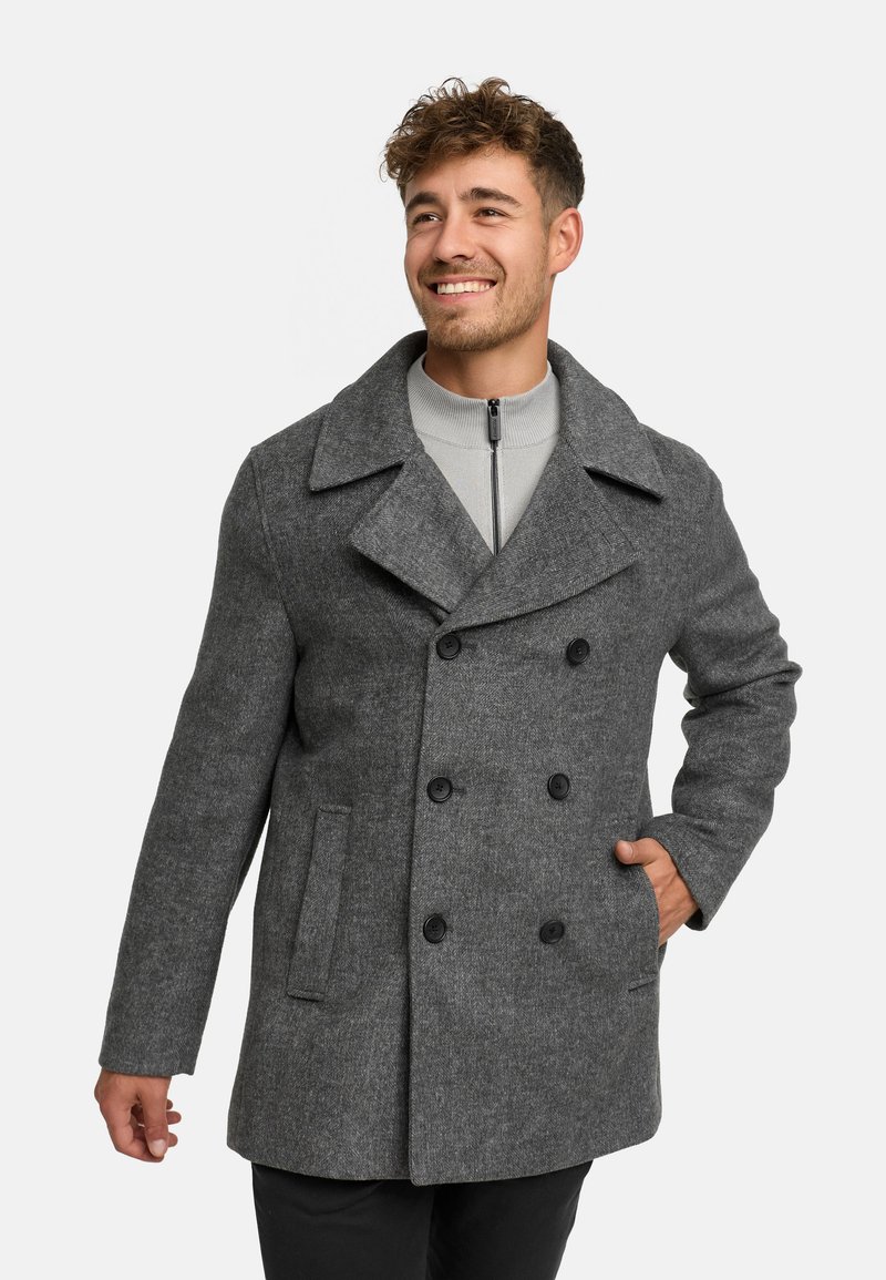 Cappotto peacoat grigio in lana con bottoni doppi, colletto a punte e tasche frontali, indossato sopra un pullover grigio con zip.