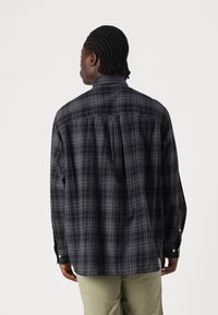 Camisa de cuadros en negro y gris de manga larga con un ajuste relajado, puños con botones y un diseño de yugo. Tela suave con un patrón de cuadros.