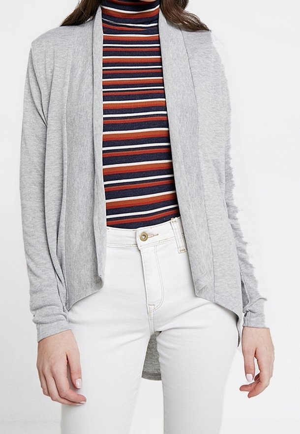 Femme portant un cardigan gris clair ouvert sur un col roulé rayé bleu marine, rouge et blanc, associé à un pantalon blanc taille haute.