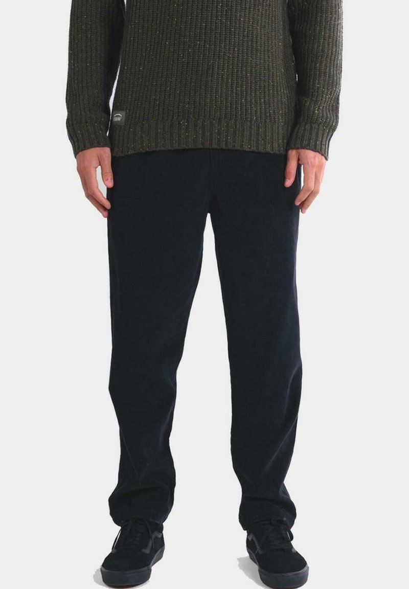 Pantalones de pana azul marino oscuro con un corte recto, combinados con un suéter de punto verde oliva texturizado. Detalles del material y acentos de estilo sutiles visibles.