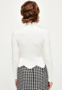 Biały prążkowany top z wysokim dekoltem i falbaniastym wykończeniem, zestawiony z spódnicą w wzór houndstooth w czarno-białym kolorze.
