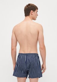 Șorturi de înot blue navy cu dungi, fabricate dintr-un material ușor, cu un elastic în talie și dungi verticale albe. Vedere din spate a unui model.