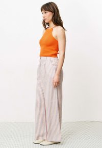 Oranje geribde tanktop gecombineerd met hooglopende, wijdvallende broek met verticale strepen in blauw, oranje en wit. Soepele textuur, casual pasvorm.