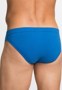 Slip in cotone blu con vita morbida, texture liscia e minimo dettaglio di cucitura, visti da dietro.