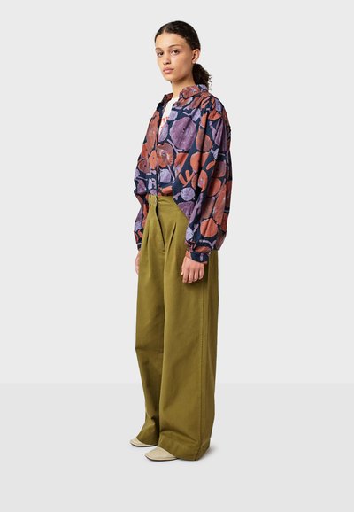 Camicia a fantasia floreale in blu scuro, con tonalità di viola e ruggine, abbinata a pantaloni a vita alta verdi oliva a gamba larga.