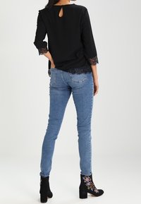 Top nero con maniche in pizzo e dettaglio chiave sul retro, abbinato a jeans skinny in denim azzurro chiaro e stivali alla caviglia neri ricamati.