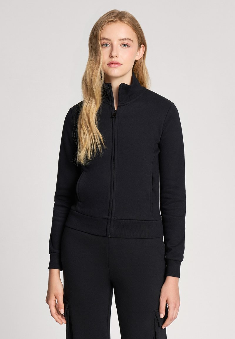 Felpa nera con zip realizzata in morbido tessuto, caratterizzata da un colletto alto, maniche lunghe e una silhouette aderente con polsini e orlo a coste.