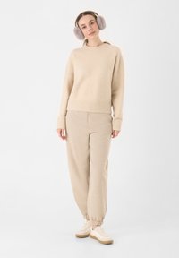 Beige gebreide trui met geribde onderkant en manchetten in combinatie met bijpassende taps toelopende sweatpants. Grijze oorkappen en lichte sneakers maken de outfit compleet.