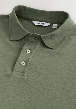 Olivengrøn polo skjorte lavet af tekstureret stof, der har en krave, tre hvide knapper og et mærke indeni med brandnavnet "NEXT."