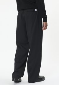 Čierne nohavice s širokými nohavicami vyrobené z text�úrovanej látky, s zadným štítkom so veľkosťou. Ďalšie detaily zahŕňajú prispôsobené švy a čistý finiš.