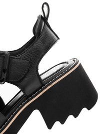 Černá kožená platformová sandála s nastavitelnou přezkou, silnou podrážkou s vroubkovaným vzorkem a šitím podél okraje podrážky.