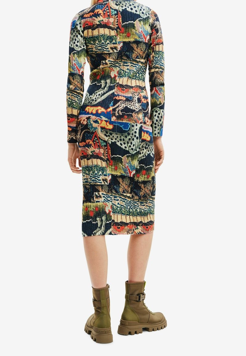 Femme portant une robe colorée à motifs longueur genou et des bottines de combat vert olive à lacets, debout, dos face au spectateur.